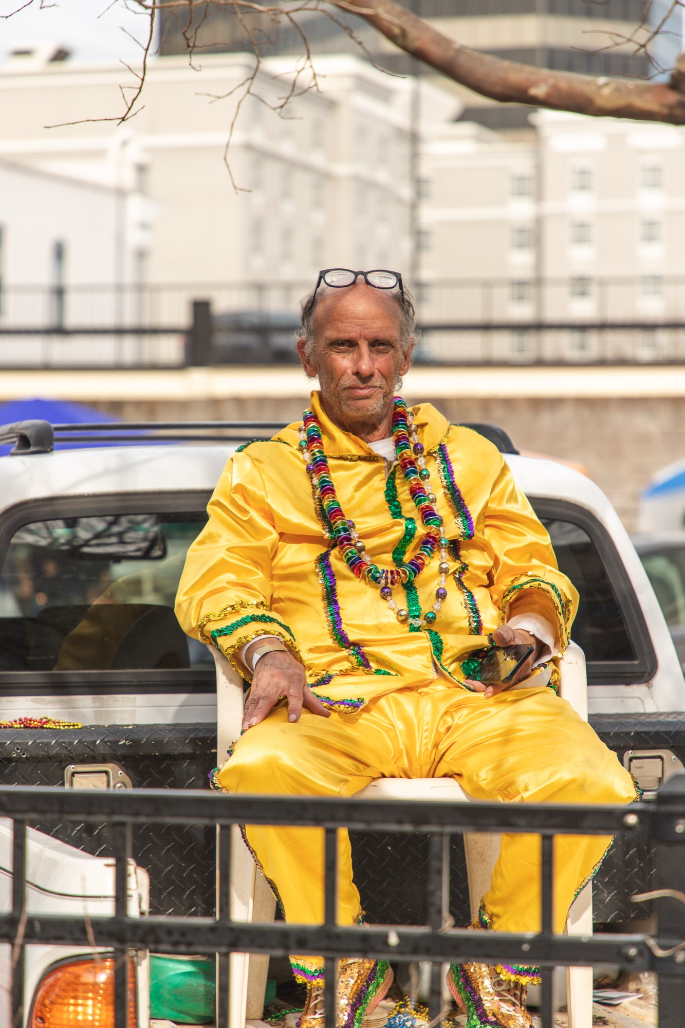 A man in a yellow satin Mardi Gras suit waits in a plastic chair in a truck bed